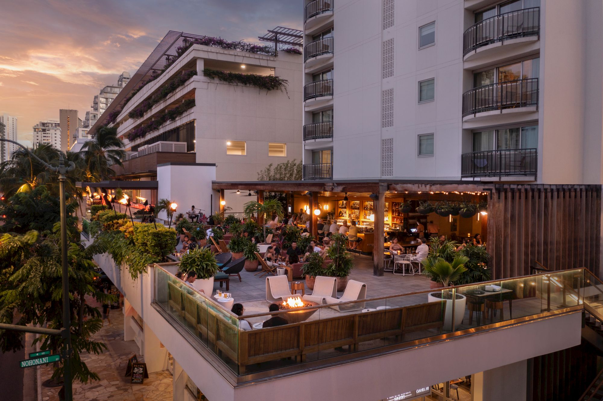 A stylish rooftop restaurant and lounge perched on a multi-story building, warm lights, plants, and people dining at sunset, lively terrace vibes.
