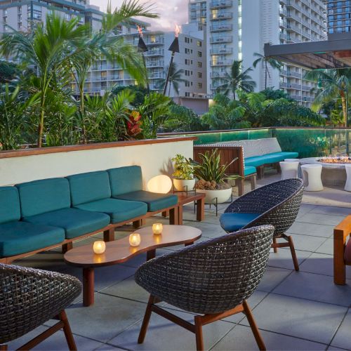 The image shows an outdoor seating area with modern furniture, plants, and cityscape views, creating a relaxing atmosphere at dusk.